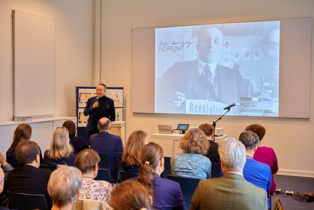 Blick in das Forum am Tag der Eröffnung. Neben dem stellvertretenden Direktor Olaf Eigenbrodt ist ein Teil des Publikums sowie ein Bild vom Namensgeber Carl von Ossietzky zu sehen.